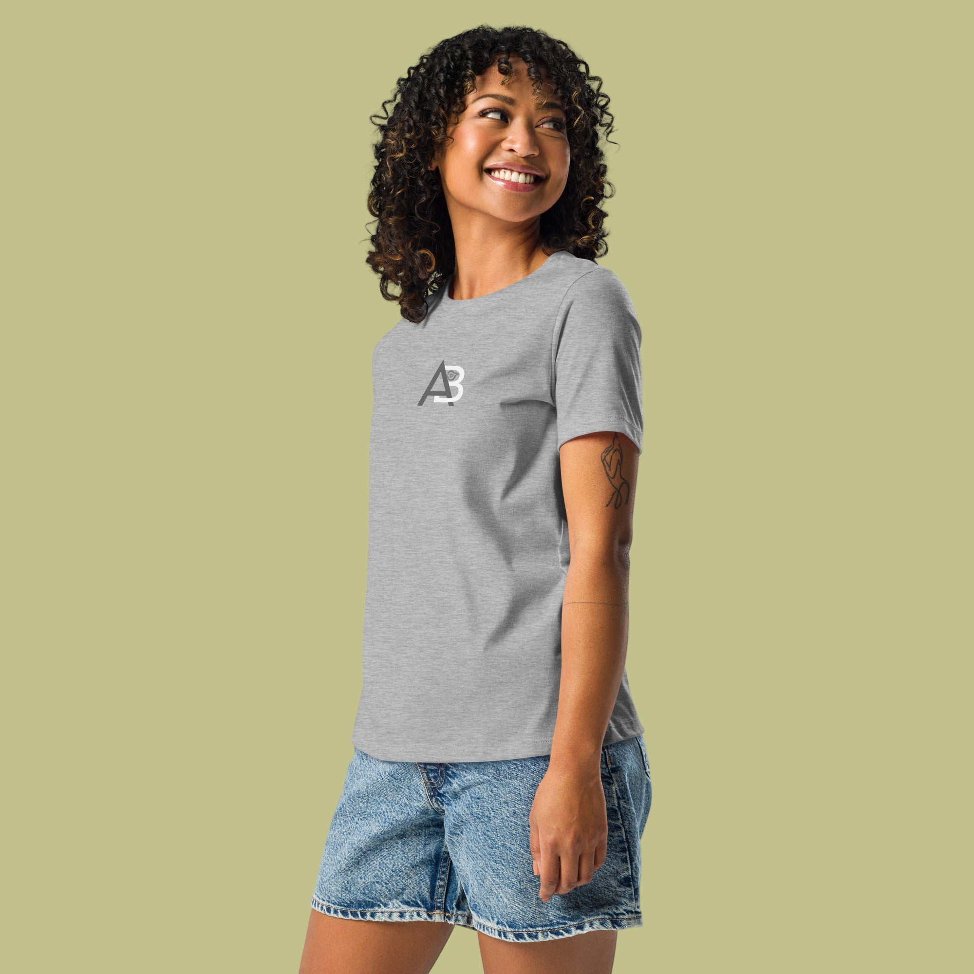 Woman wearing a gray t-shirt with a logo and denim shorts on a green background