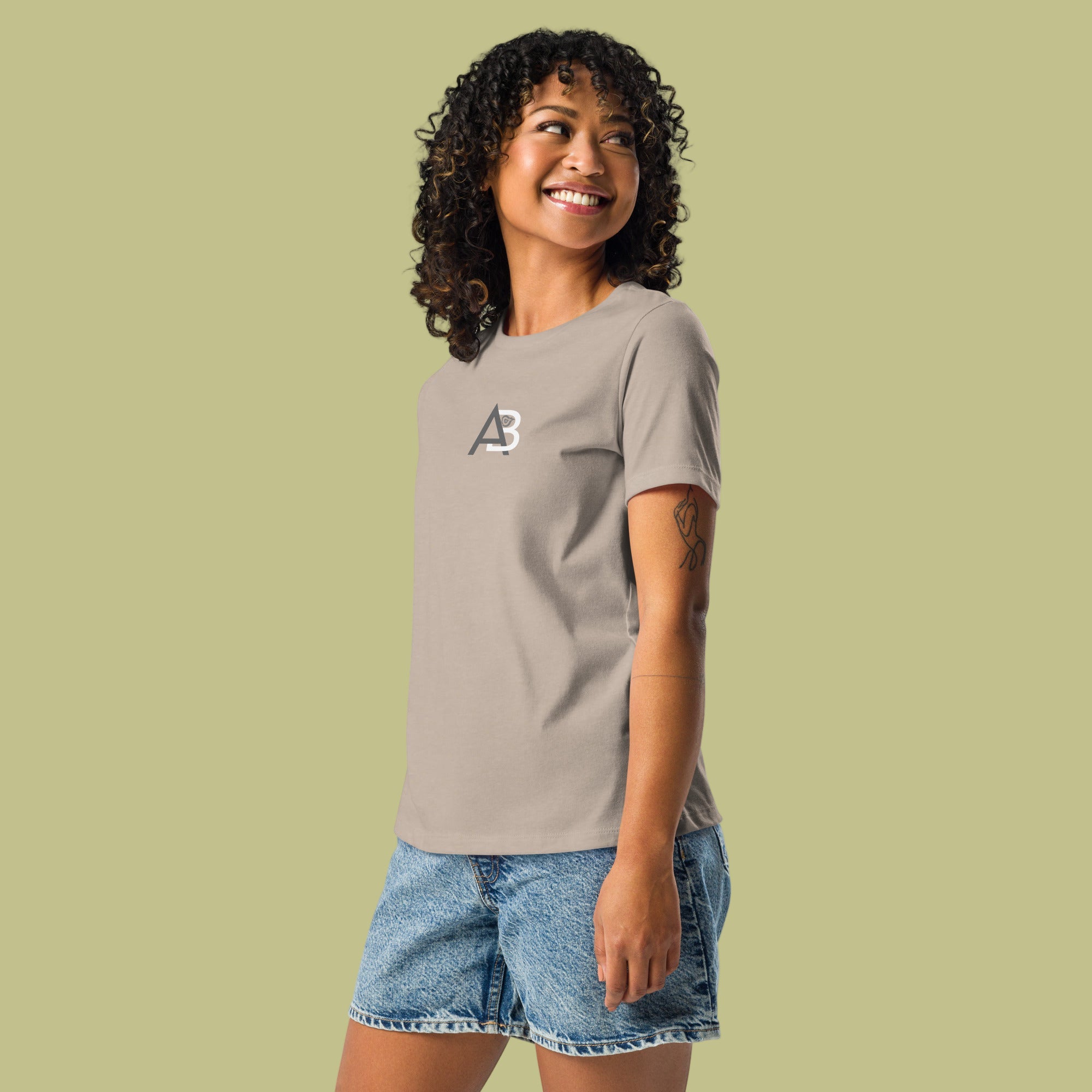 Woman wearing a gray t-shirt with a logo and denim shorts on a green background